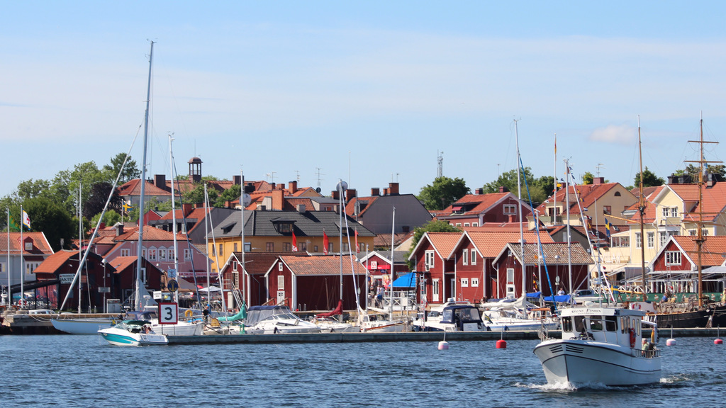 Vy över öregrunds hamn, där fiskebodar står på rad efter kajen och segelbåtar ligger anlagda vid bryggan.
